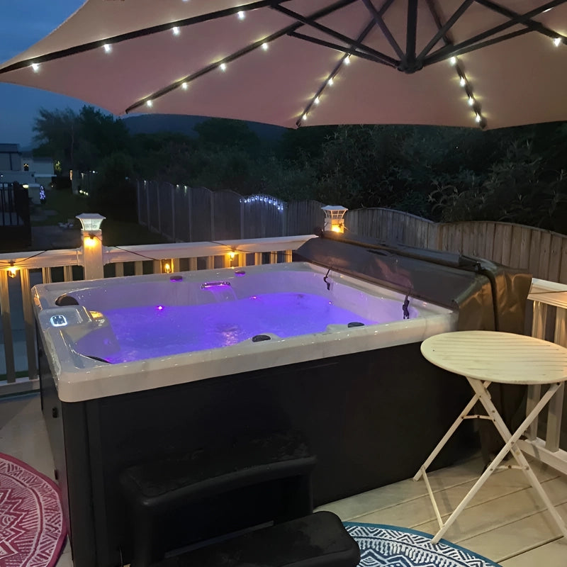 Hot tub in the garden at night with parasol with led lights attached to it.